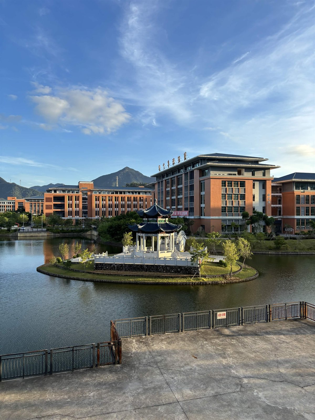 Lakeside campus landscape framed by mountains and a blue sky